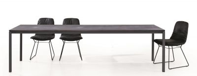 S 600 Tisch von Janua mit geölter Eichenplatte und schwarzen Stühlen vor weißem Hintergrund.